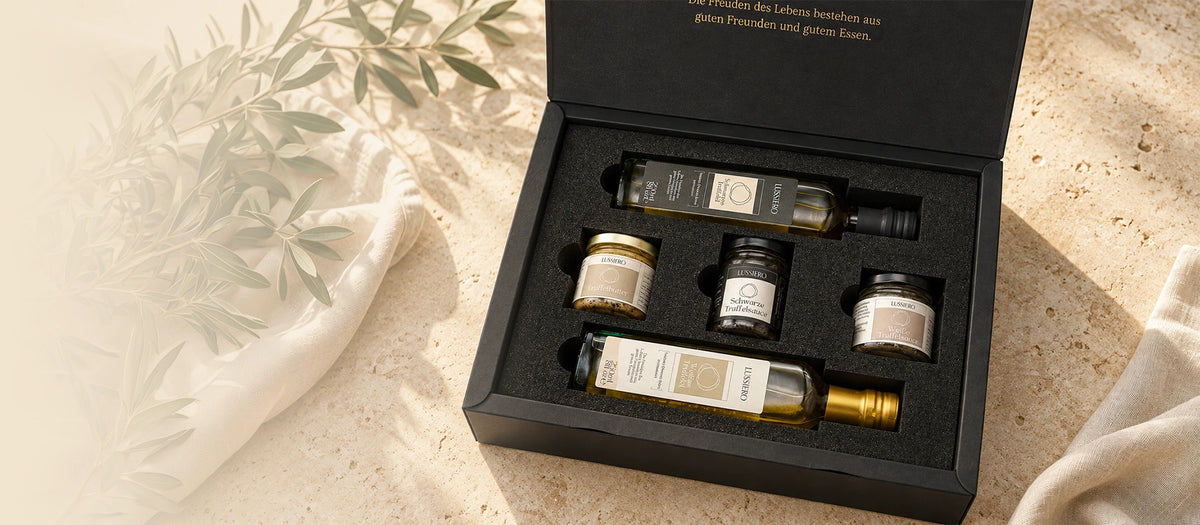Offene Lussiero Geschenkbox mit Trüffelölen, Trüffelbutter und Saucen auf warmem Stein mit Olivenzweigen und Leinen