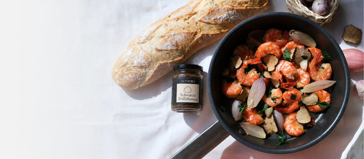 Lussiero schwarze Trüffelsauce neben einer Pfanne mit Garnelen und Trüffeln, Baguette und hellem Leinen